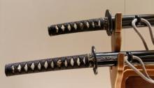 Two samurai swords sitting on a sword rack, showing intricate carvings sit