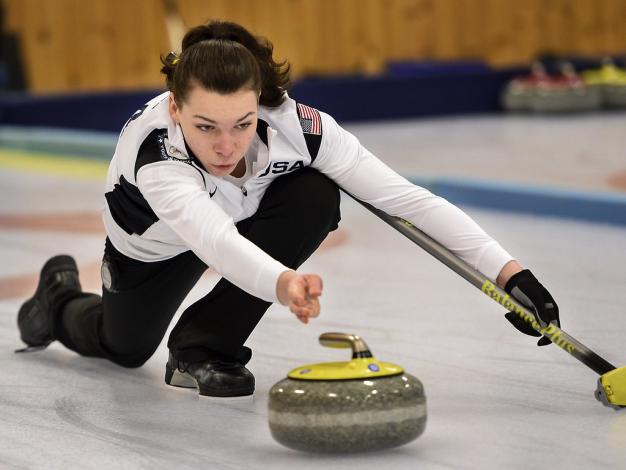 Woman launching a curling rock, kneeling on the ground with her arm outstretched