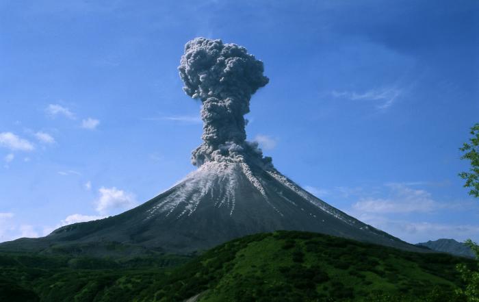 The eruption of the Karymsky Volcano in Russia on July 13, 2004. Gray smoke billowing from the top of the volcano against a blue sky.