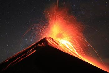 The eruption of the Fuego Volcano in Guatemala on March 3, 2013. Red lava is spewing from the top of the volcano against a black night sky.